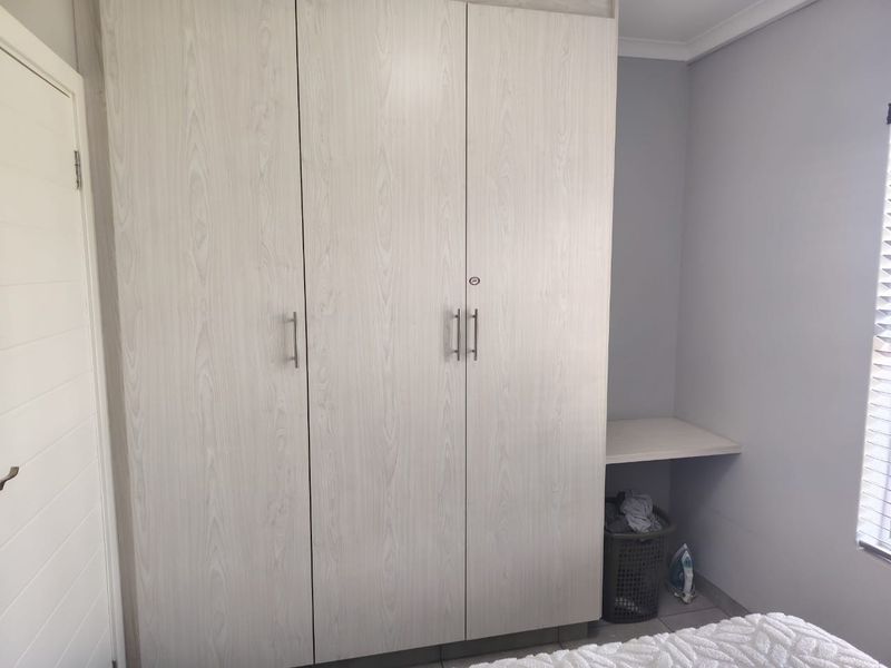 A bedroom featuring light wood-grain built-in wardrobes and a compact built-in desk area with window blinds.
