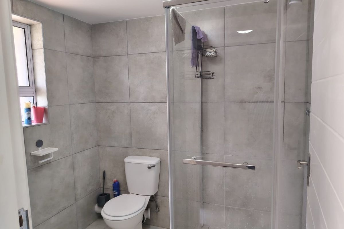 A modern bathroom featuring grey wall tiles, a glass shower enclosure, and a standard toilet.