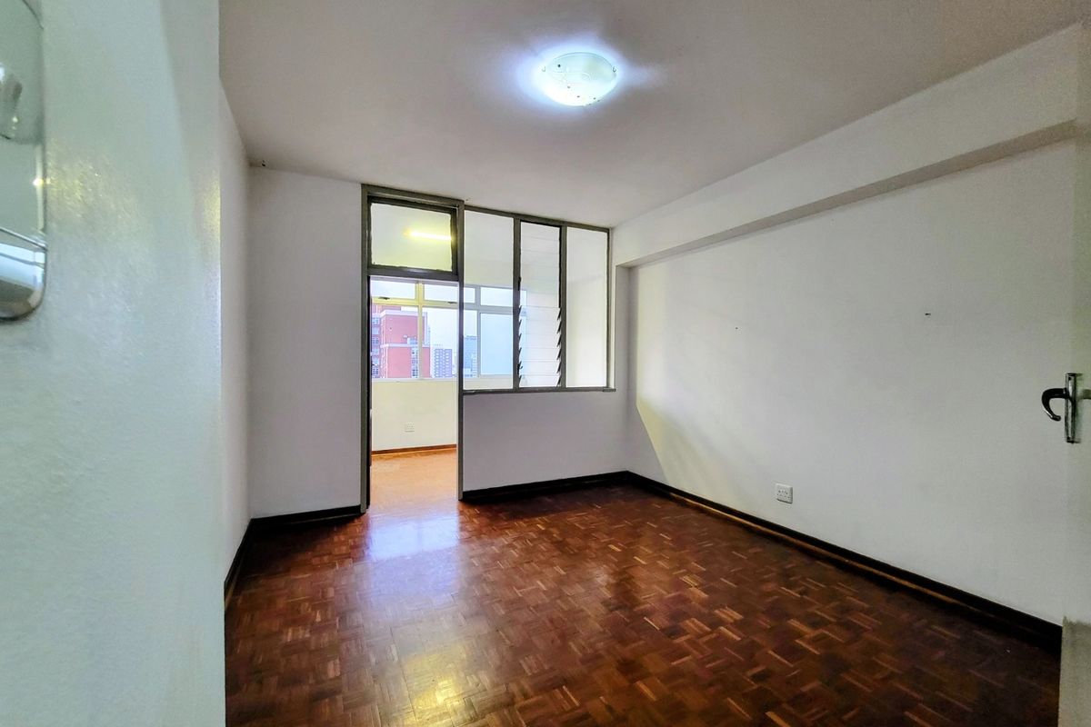 An empty bedroom featuring original parquet flooring, a glass partition wall, and a louvered window providing natural light.