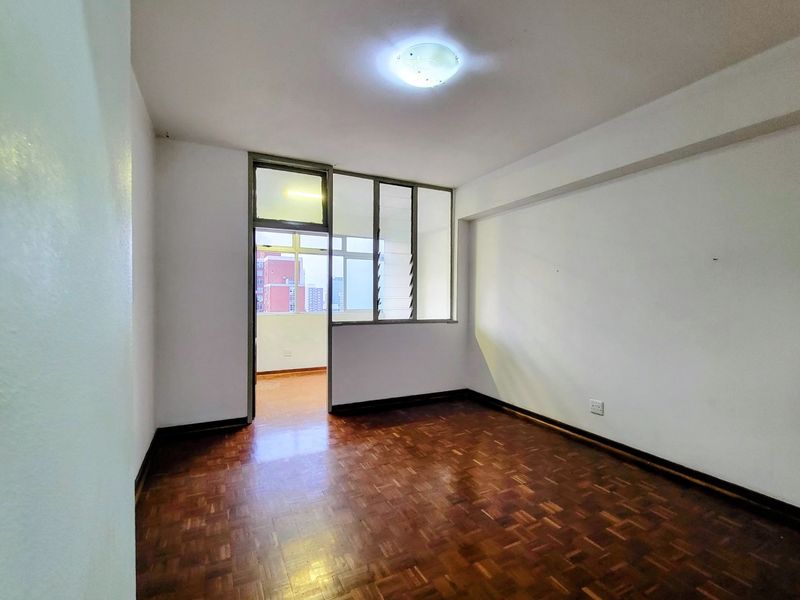 An empty bedroom featuring original parquet flooring, a glass partition wall, and a louvered window providing natural light.