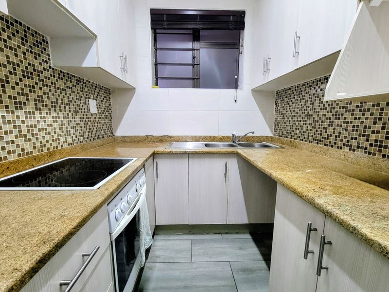 Compact kitchen featuring granite countertops, mosaic tile backsplash, built-in electric hob and oven, and ample laminate cabinetry storage.
