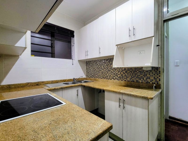 Compact kitchen featuring granite countertops, mosaic tile backsplash, built-in cabinetry, and an integrated electric hob.