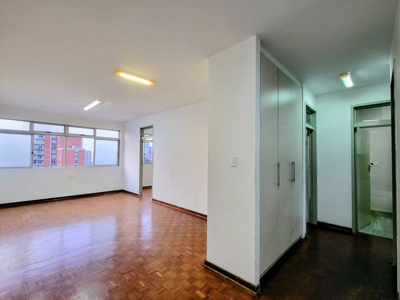 An empty living area featuring parquet flooring, built-in storage cupboards, and large windows providing natural light and urban views.