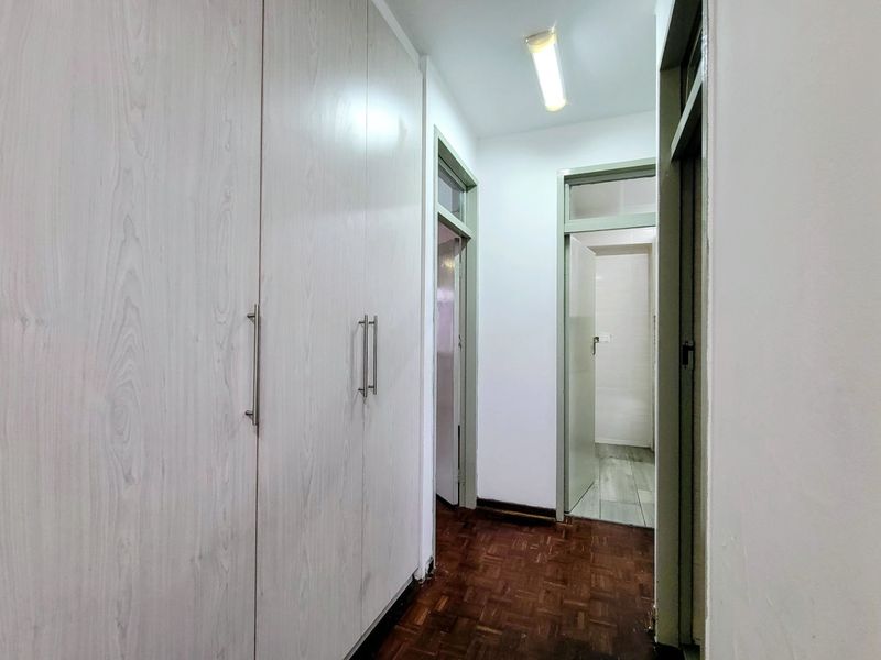 A functional hallway featuring built-in storage cupboards and classic parquet flooring, providing access to adjacent rooms within the apartment.
