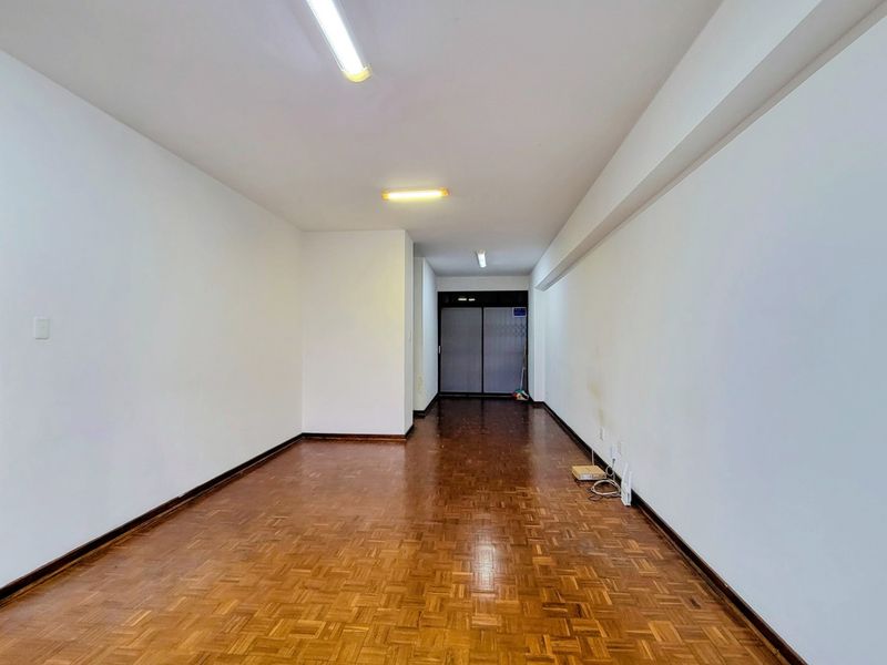 An empty hallway featuring parquet flooring, fluorescent lighting, and a sliding security gate at the end.