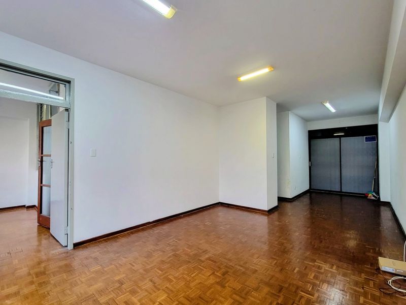An empty living area featuring traditional parquet flooring, neutral walls, and built-in storage cupboards, offering a blank canvas for interior design.