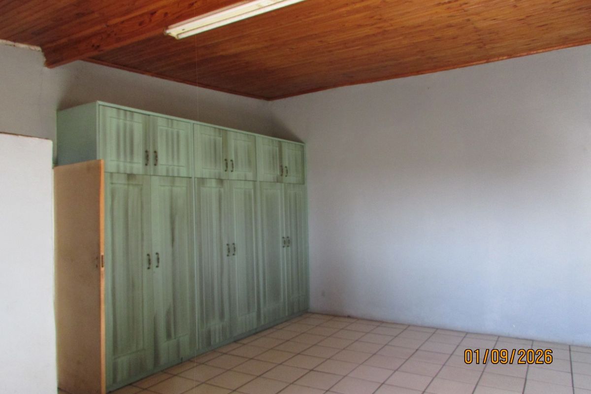 A vacant bedroom featuring tiled flooring, a timber ceiling, and built-in cupboards in need of cosmetic updates.