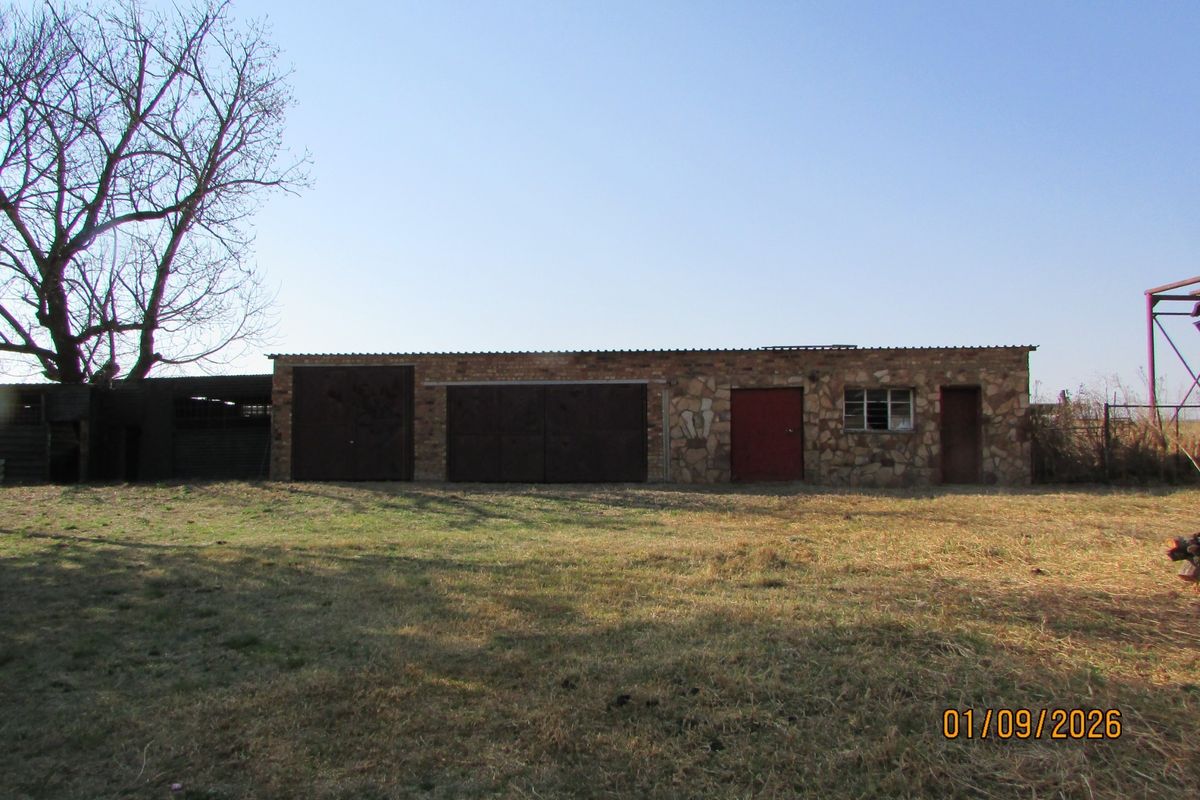 A rustic farm outbuilding featuring stone masonry walls and multiple metal access doors, set within a large open field.