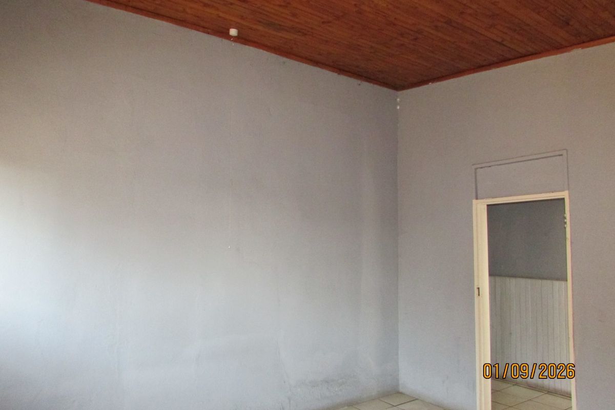 An empty living area featuring a timber ceiling, tiled flooring, and neutral wall finishes, providing a blank canvas for potential renovation.