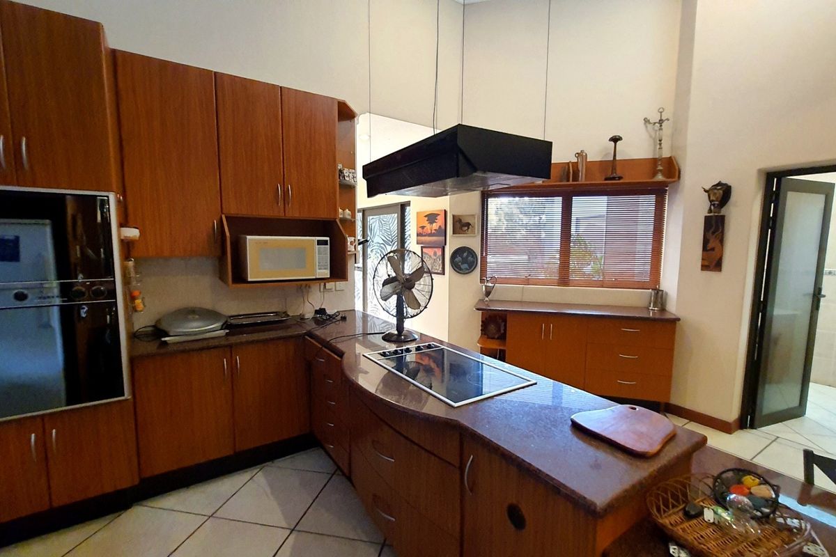 A spacious kitchen featuring wooden cabinetry, granite countertops, a built-in oven, and a central island with a hob and overhead extractor fan.