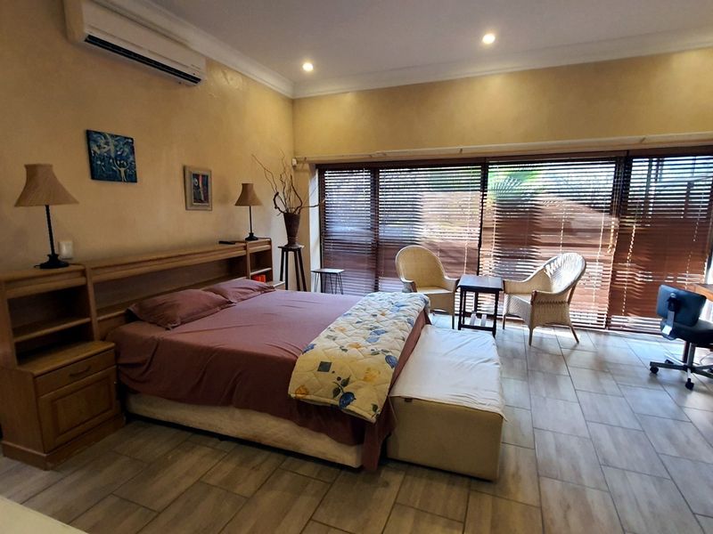 Spacious bedroom featuring tiled flooring, recessed lighting, a wall-mounted air conditioning unit, and large sliding glass doors with venetian blinds.