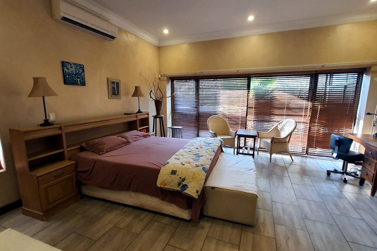 Spacious bedroom featuring tiled flooring, recessed lighting, a wall-mounted air conditioning unit, and large sliding glass doors with venetian blinds.