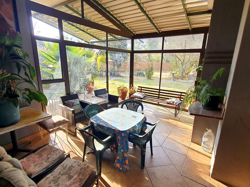 Enclosed patio area featuring tiled flooring, large glass windows, and a metal roof structure, offering a bright space with views of the garden.