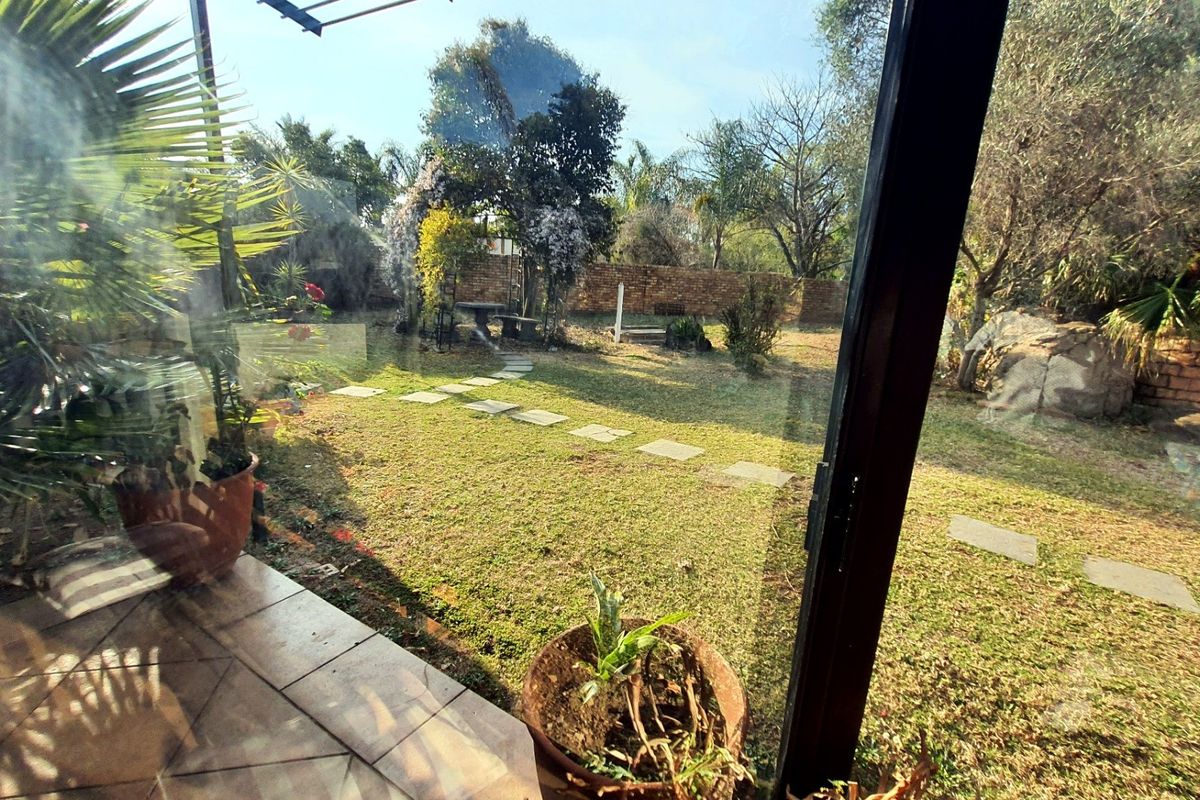 A view of a rear garden with a tiled patio, stone stepping stones, and a brick boundary wall, captured through a glass door.