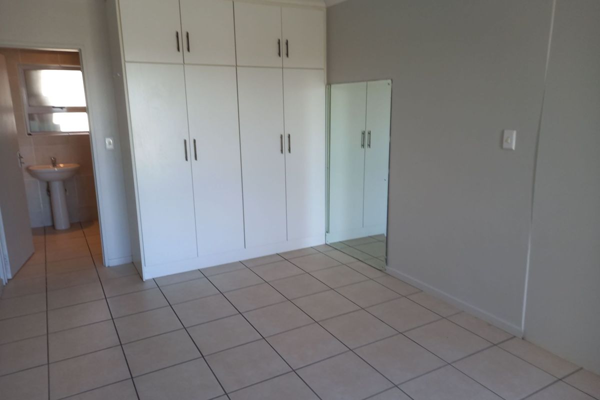 A clean, empty bedroom featuring built-in cupboards, tiled flooring, and direct access to an en-suite bathroom.