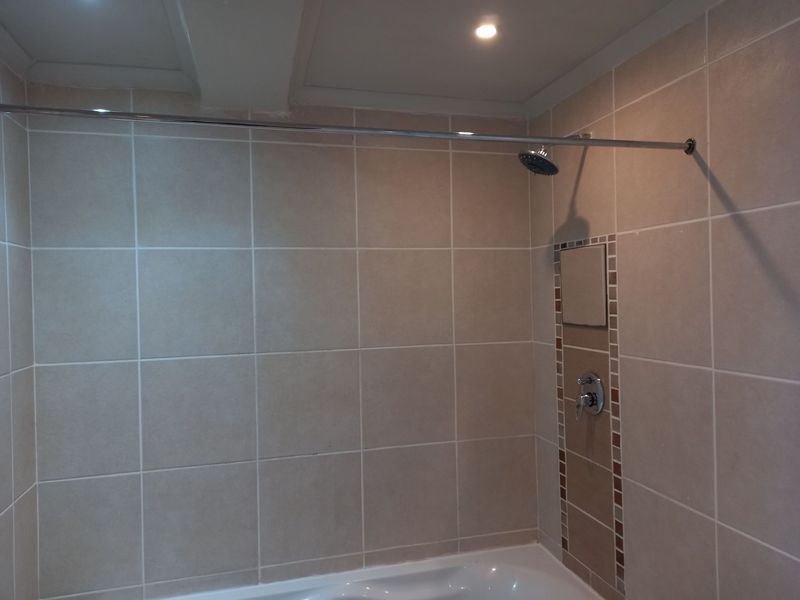 A functional bathroom shower area featuring neutral wall tiles, a built-in shower mixer, and a shower head with a curtain rod.