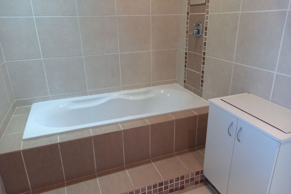 A clean bathroom featuring a built-in bathtub with tiled surround and a white vanity cabinet.