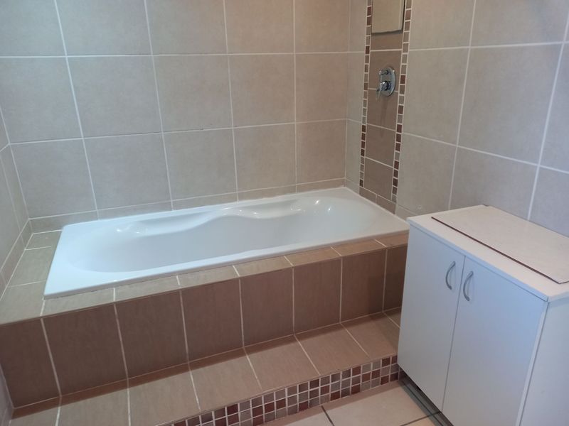 A clean bathroom featuring a built-in bathtub with tiled surround and a white vanity cabinet.