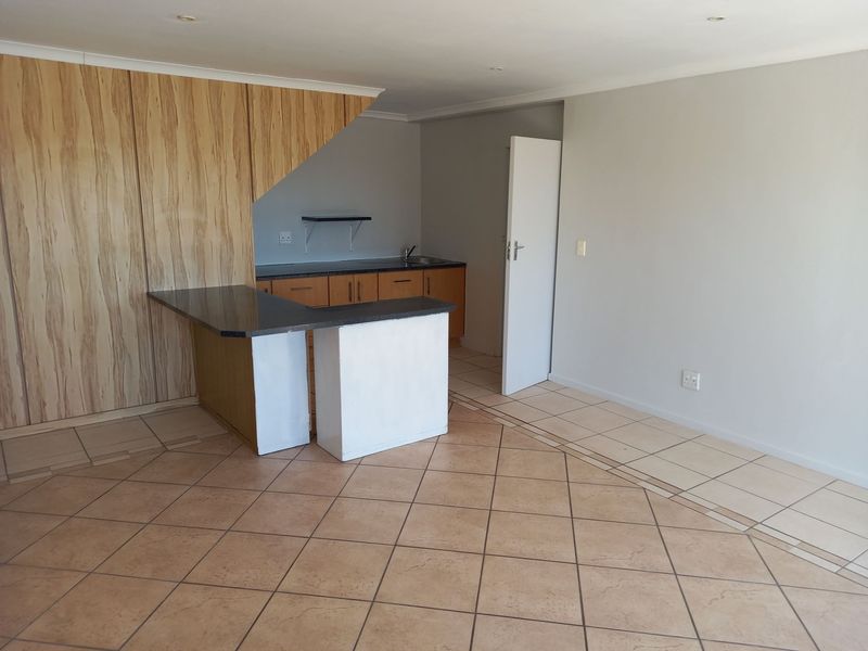 An open-plan living and kitchen area featuring tiled flooring, built-in cabinetry, and a breakfast counter, offering a functional and versatile space.