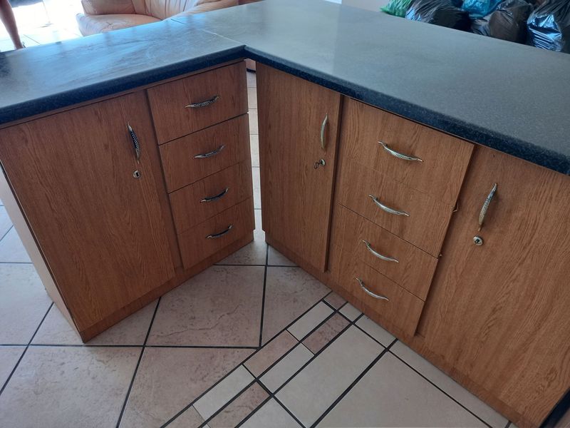 A kitchen island featuring wood-look laminate cabinetry, dark countertops, and patterned ceramic floor tiles.