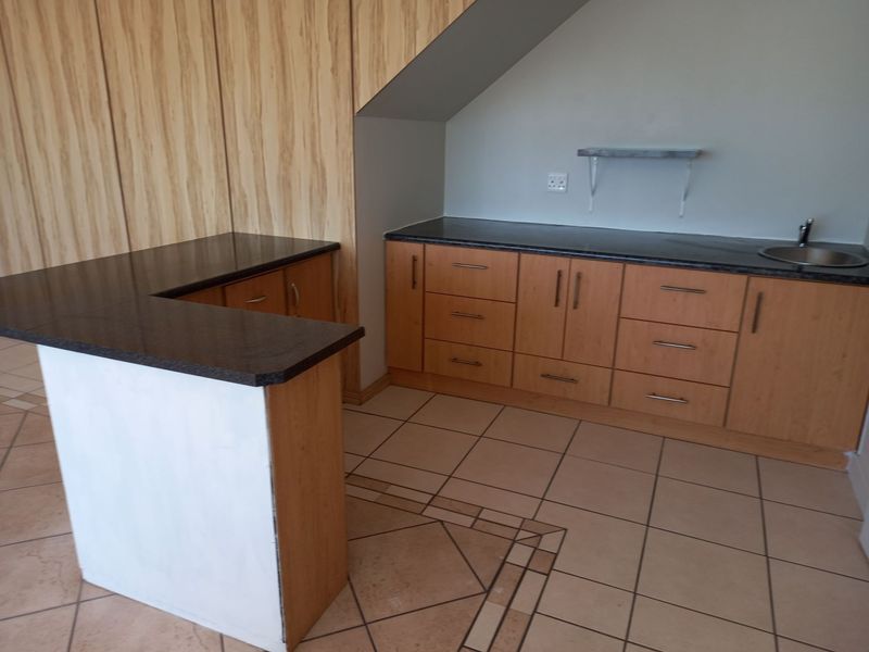 A functional kitchen area featuring light wood cabinetry, dark granite countertops, a breakfast bar, and tiled flooring in an open-plan layout.