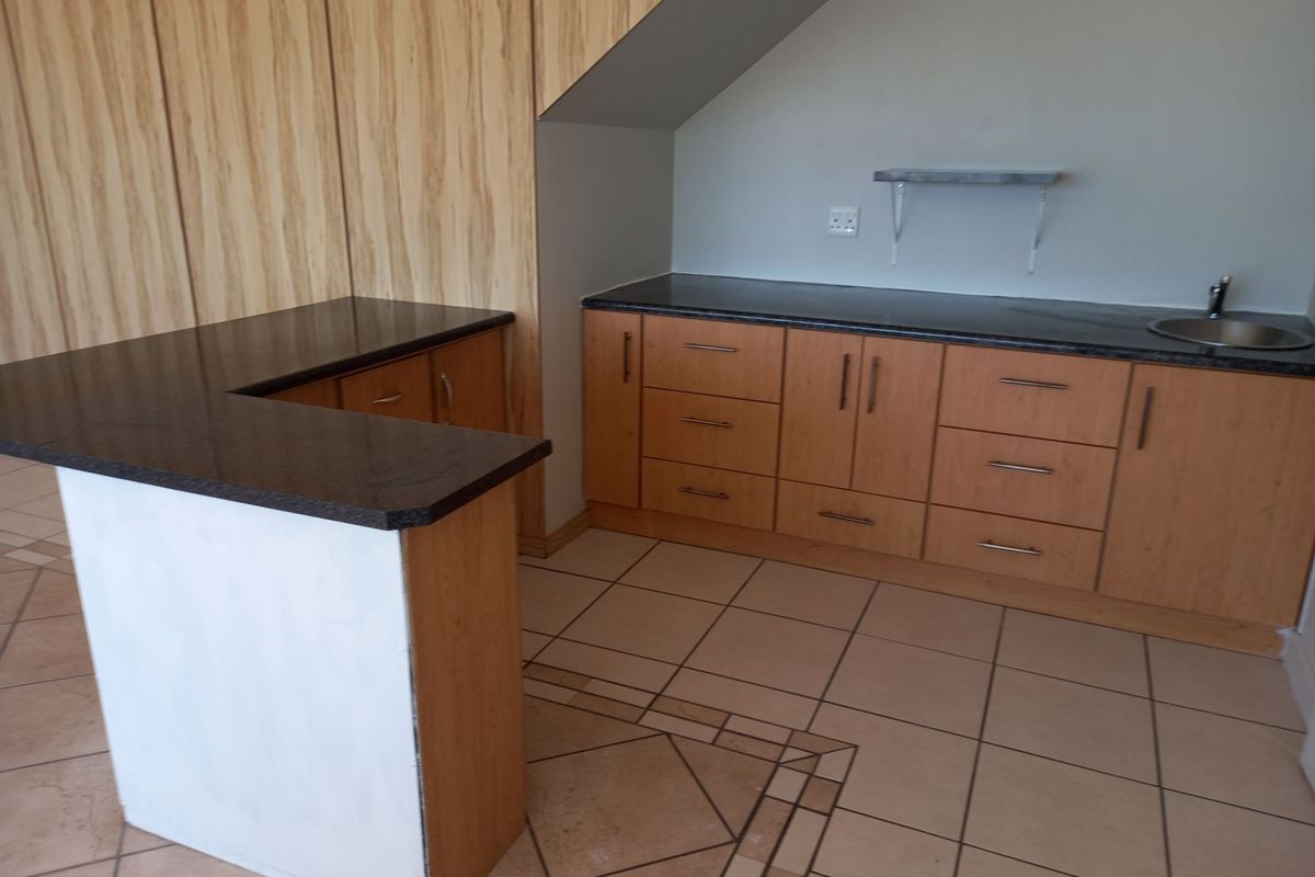 A functional kitchen area featuring light wood cabinetry, dark granite countertops, a breakfast bar, and tiled flooring in an open-plan layout.