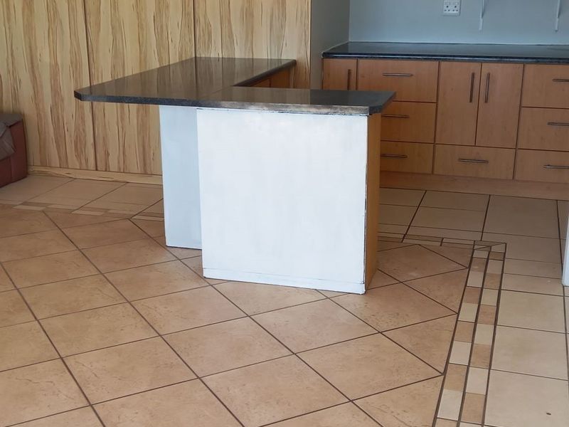 A kitchen area featuring built-in wooden cabinetry, a stone-topped island, and decorative ceramic floor tiling.