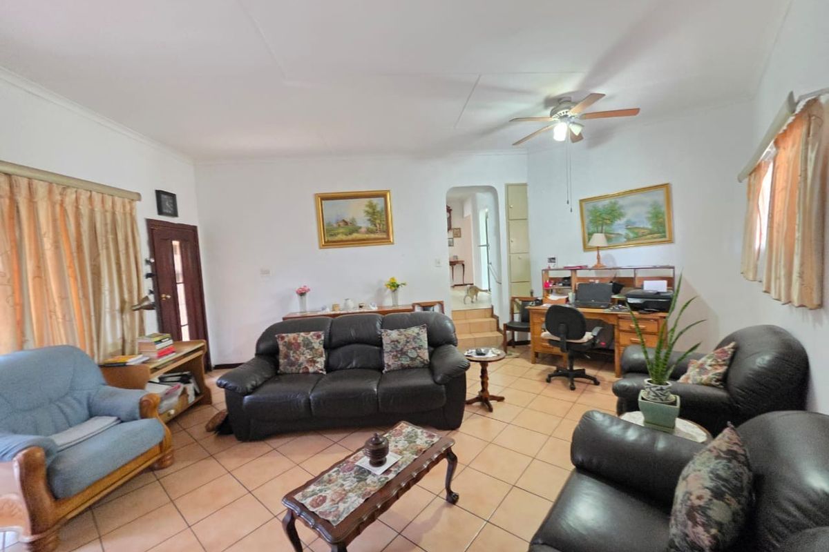 A spacious living room featuring tiled flooring, a ceiling fan, and an archway leading to adjacent areas of the home.