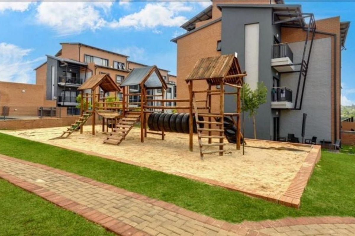 Communal outdoor area featuring a well-maintained children's playground with sand pit, set against a modern multi-story apartment complex with paved walkways.