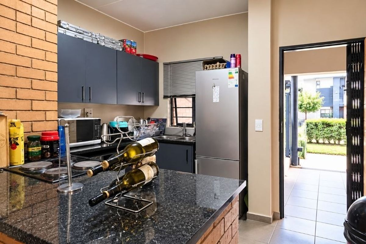 A functional kitchen featuring granite countertops, dark cabinetry, and a brick feature wall, with direct access to an outdoor patio area.