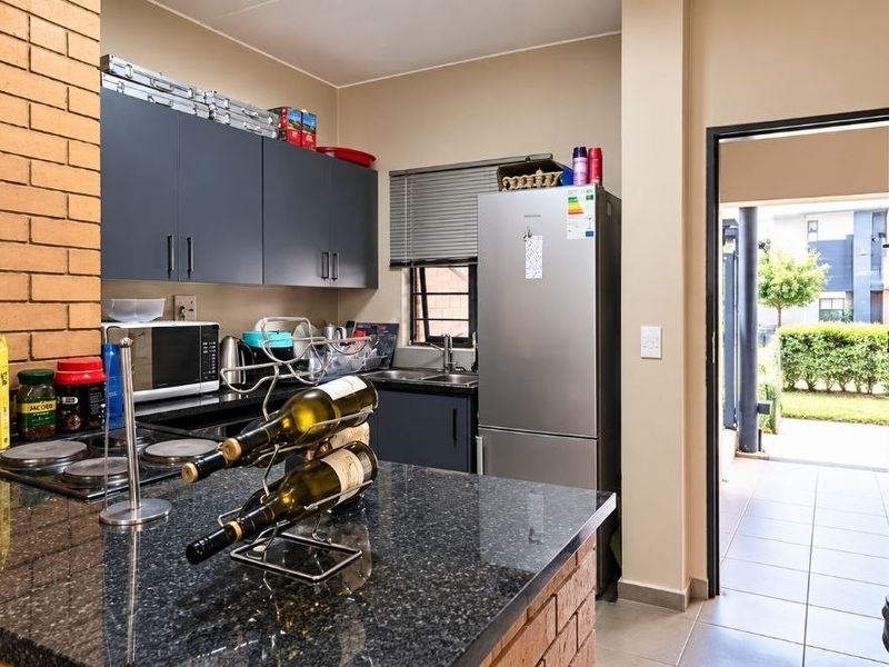 A functional kitchen featuring granite countertops, dark cabinetry, and a brick feature wall, with direct access to an outdoor patio area.