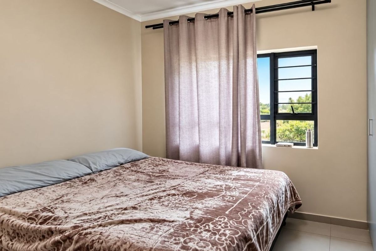 A well-maintained bedroom featuring tiled flooring, a built-in wardrobe, and an aluminium-framed window with natural light.