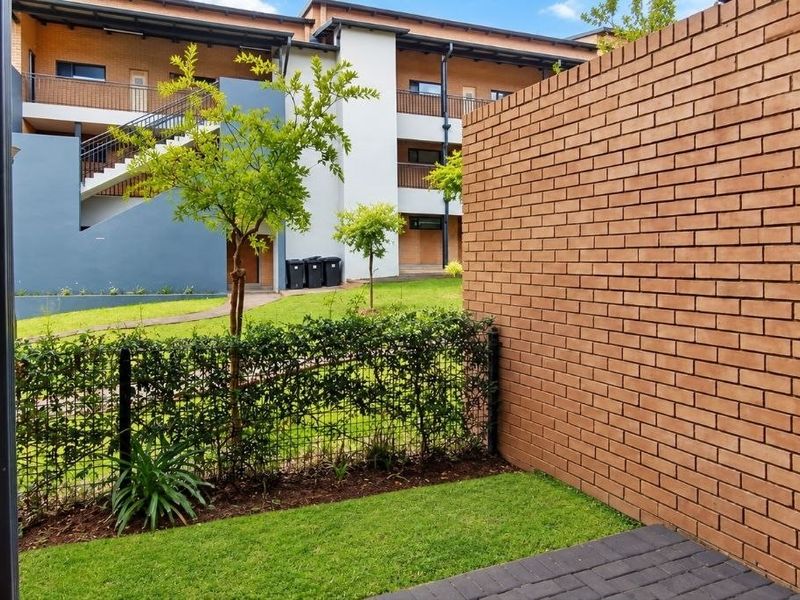 A private rear patio area featuring a brick boundary wall, paved flooring, and a small lawn overlooking the apartment complex grounds.