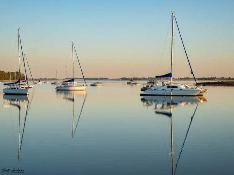 A serene view of sailboats anchored in calm, reflective waters, highlighting the peaceful coastal or lakeside setting of the property.