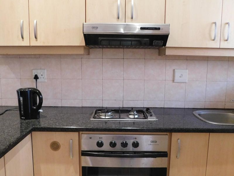 A functional kitchen featuring laminate cabinetry, granite countertops, a gas hob, built-in oven, and a stainless steel sink with tiled backsplash.