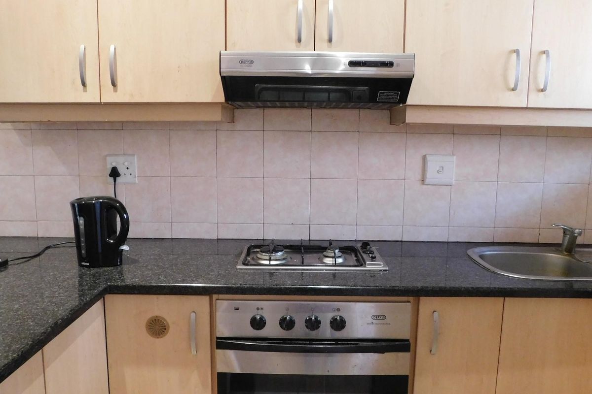 A functional kitchen featuring laminate cabinetry, granite countertops, a gas hob, built-in oven, and a stainless steel sink with tiled backsplash.