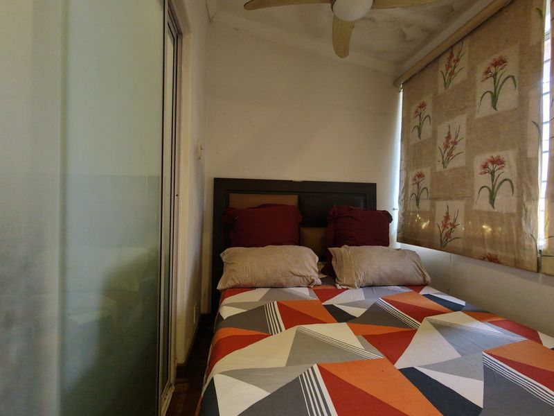 A compact bedroom featuring a ceiling fan and sliding door access, showing visible signs of ceiling water damage.