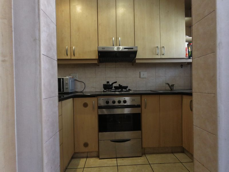 Compact kitchen featuring light wood-finish cabinetry, granite countertops, a built-in oven with extractor fan, and tiled flooring.