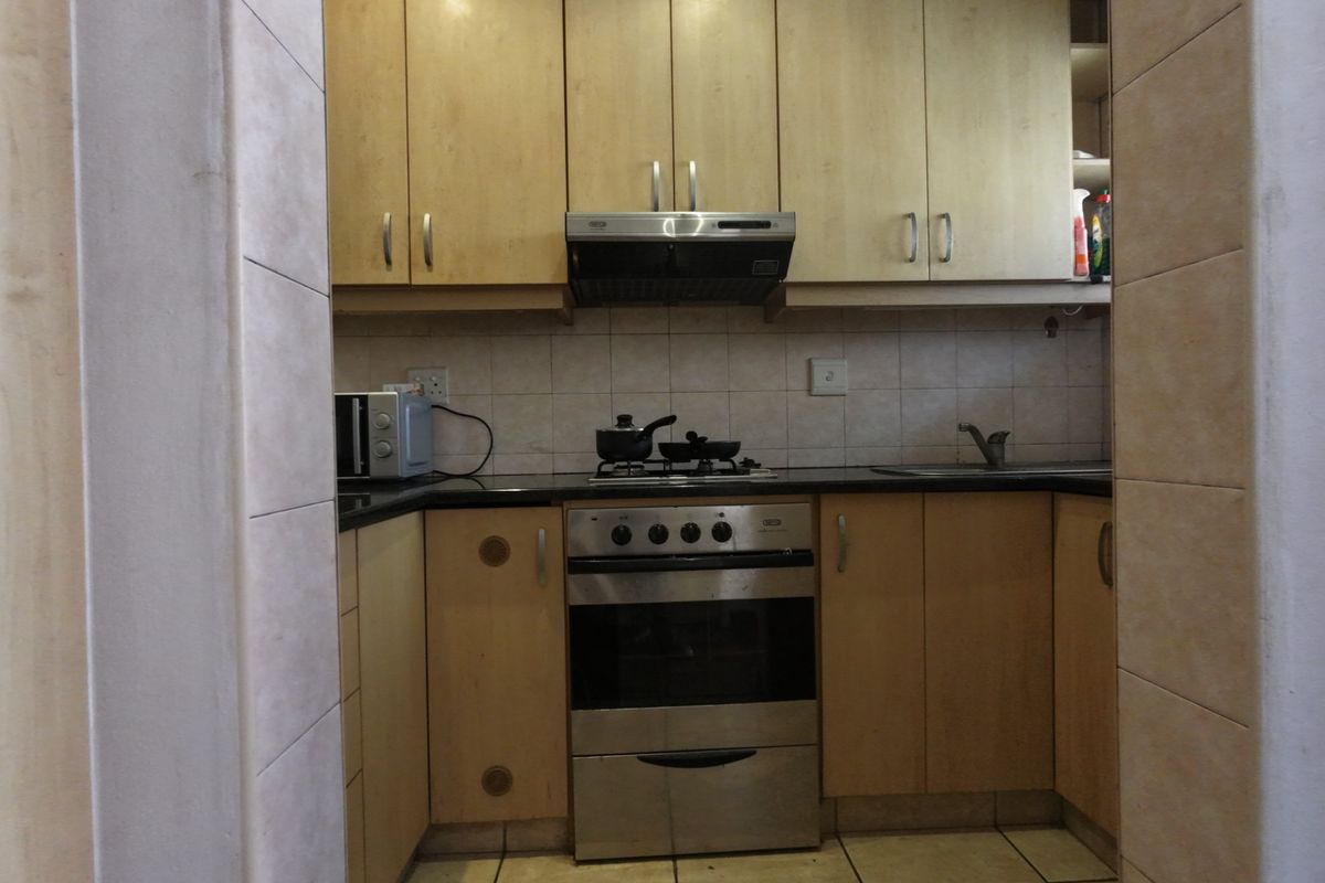 Compact kitchen featuring light wood-finish cabinetry, granite countertops, a built-in oven with extractor fan, and tiled flooring.