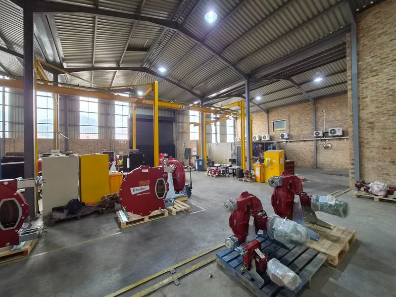 Spacious industrial warehouse facility featuring high ceilings with exposed steel trusses, concrete flooring, and an integrated overhead gantry crane system.