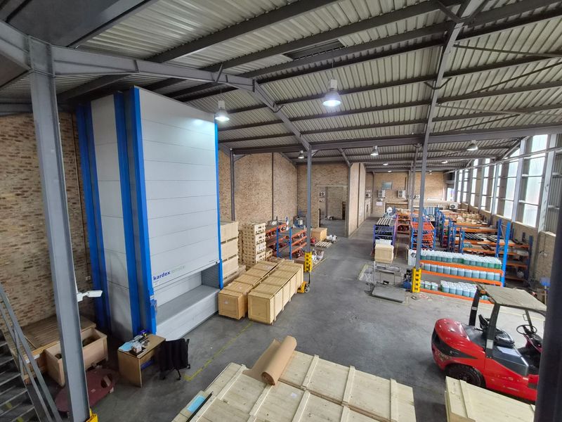 Spacious industrial warehouse featuring exposed brick walls, steel roof trusses, concrete flooring, and an automated vertical storage carousel system.