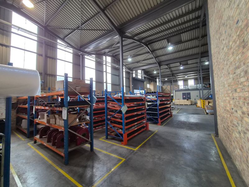 Spacious industrial warehouse featuring a steel portal frame, exposed brickwork, concrete flooring, and high-level windows providing ample natural light.