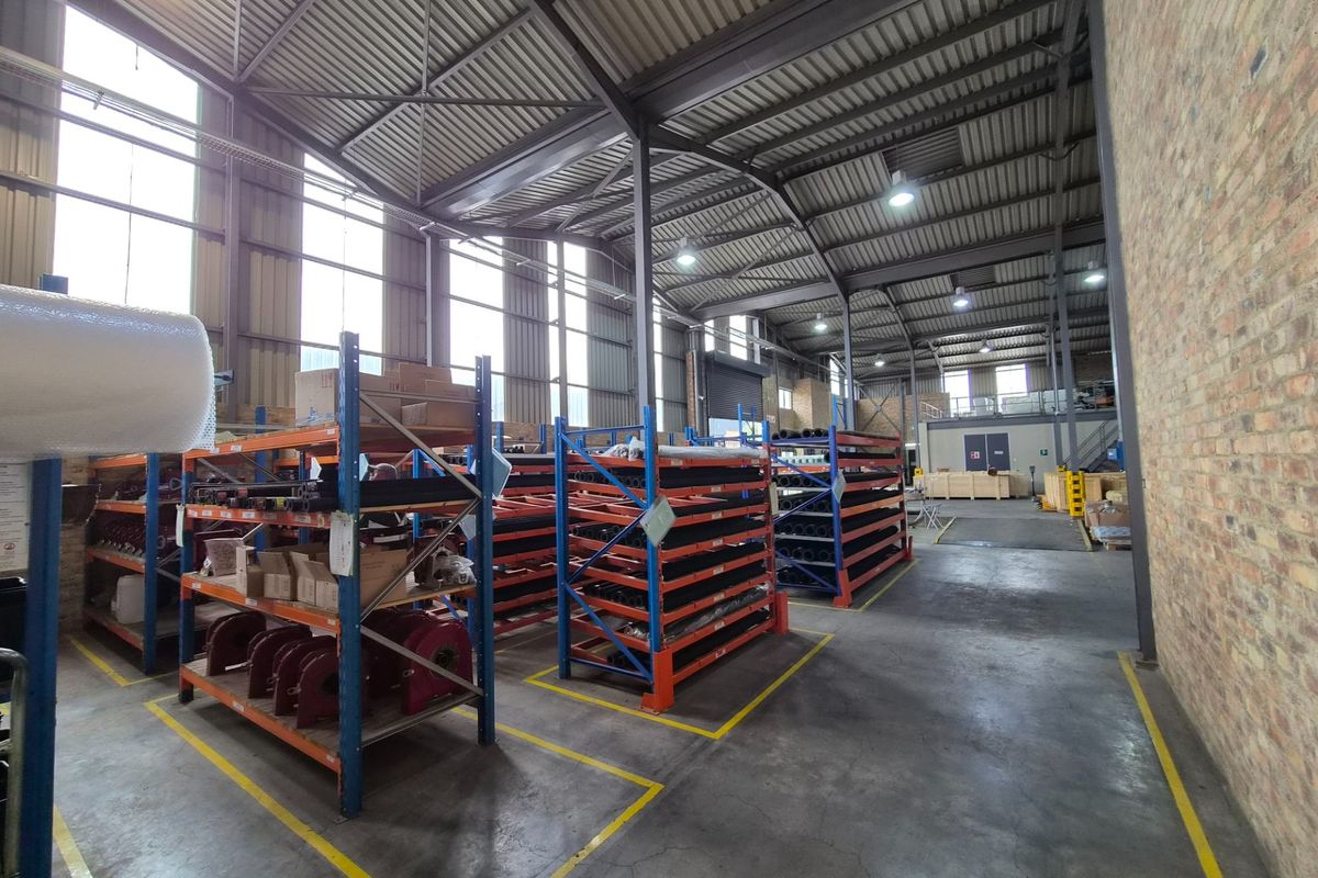 Spacious industrial warehouse featuring a steel portal frame, exposed brickwork, concrete flooring, and high-level windows providing ample natural light.