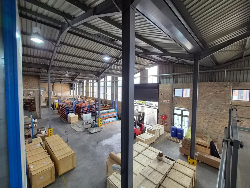Spacious industrial warehouse featuring high ceilings, exposed brick walls, concrete flooring, and large roller shutter access, suitable for storage or manufacturing operations.