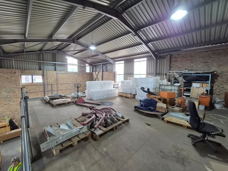 Spacious industrial warehouse area featuring exposed steel roof trusses, corrugated metal roofing, and durable concrete flooring, suitable for storage or light manufacturing operations.