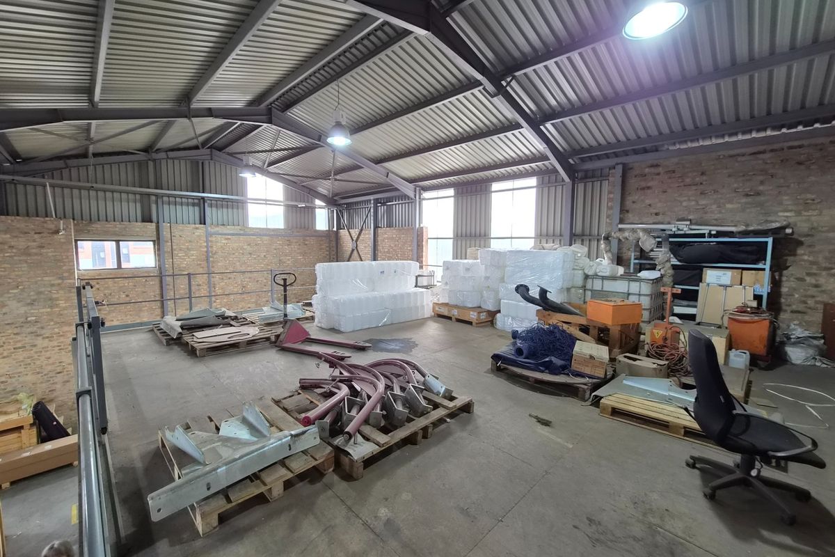 Spacious industrial warehouse area featuring exposed steel roof trusses, corrugated metal roofing, and durable concrete flooring, suitable for storage or light manufacturing operations.