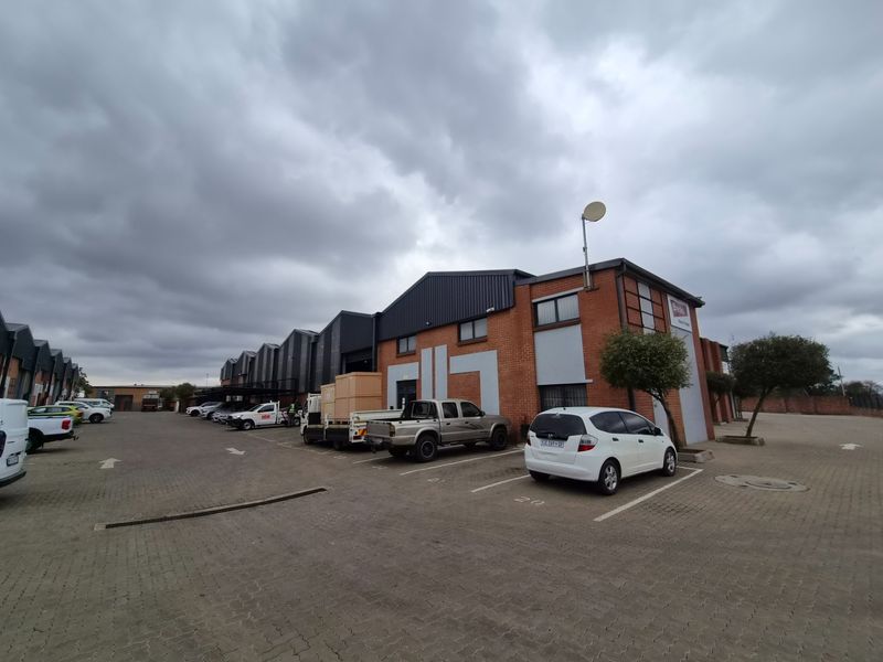 Exterior view of an industrial warehouse complex featuring a brick facade, metal roofing, and an expansive paved parking area for commercial use.
