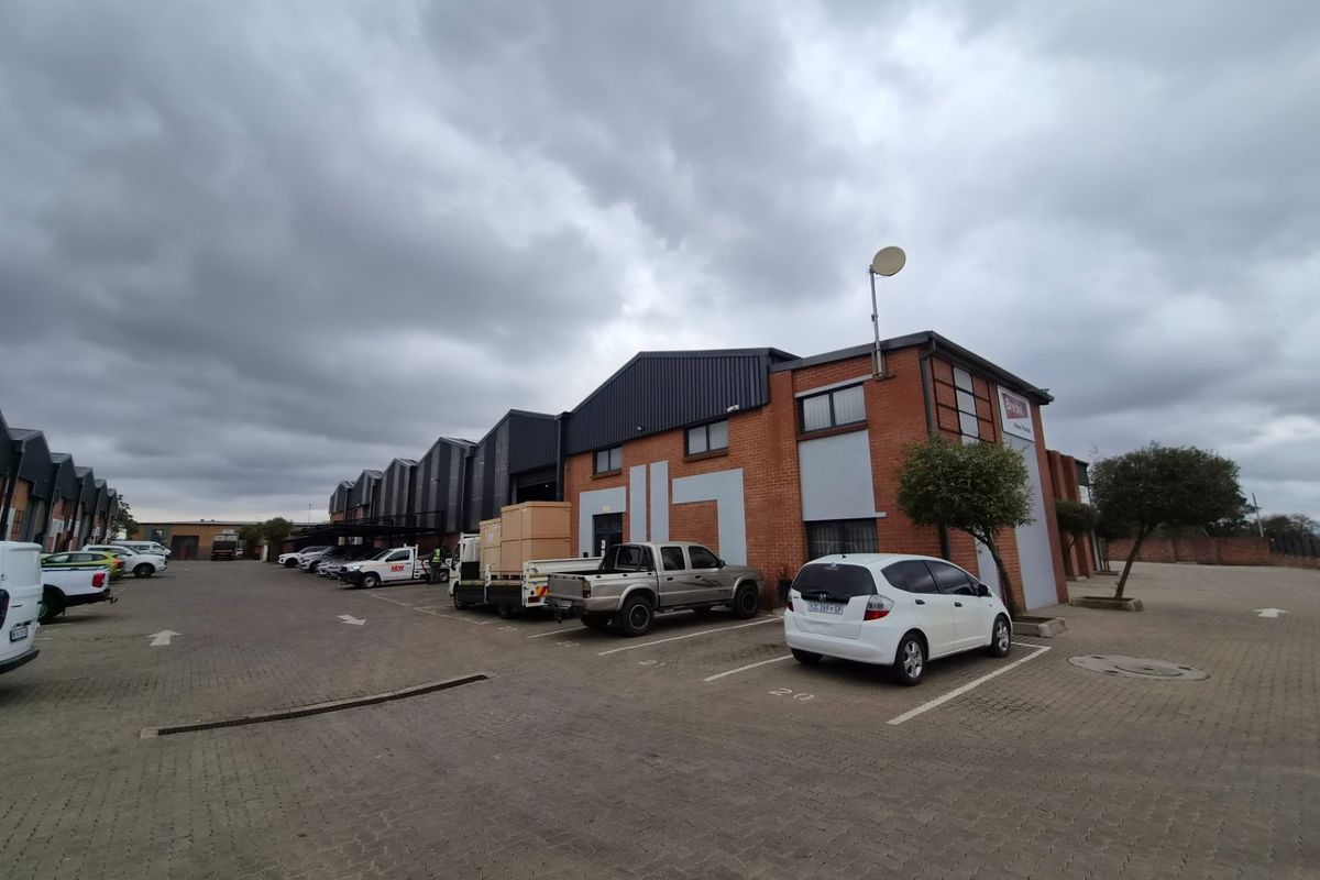 Exterior view of an industrial warehouse complex featuring a brick facade, metal roofing, and an expansive paved parking area for commercial use.