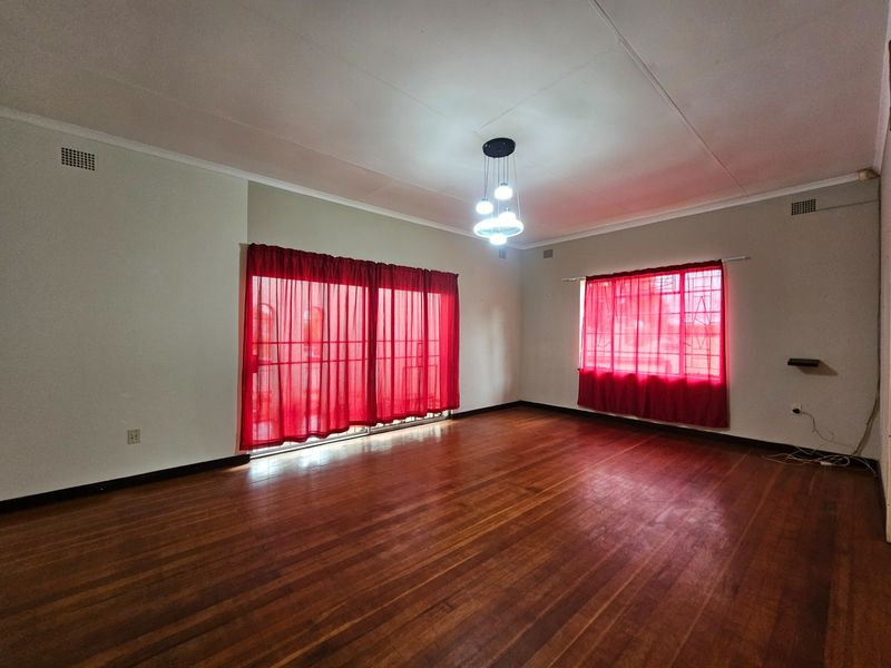 Spacious living room featuring polished hardwood flooring, a modern pendant light fixture, and large windows with security bars.