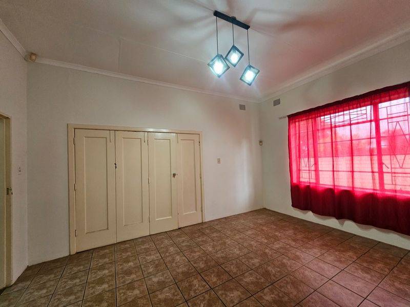 A vacant bedroom featuring tiled flooring, built-in cupboards, and a modern geometric ceiling light fixture.